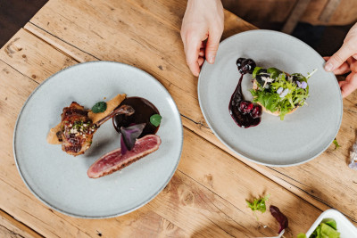 Two plated dishes. Two hands reaching for one of them.