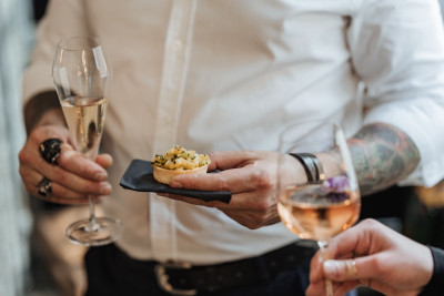 Event guest holding finger food in one hand and a glass of sparkling wine in the other